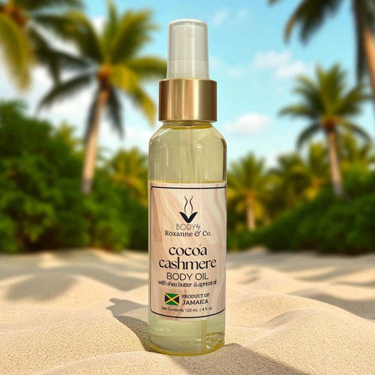 Bottle of cocoa cashmere body oil on sand with palm trees in the background