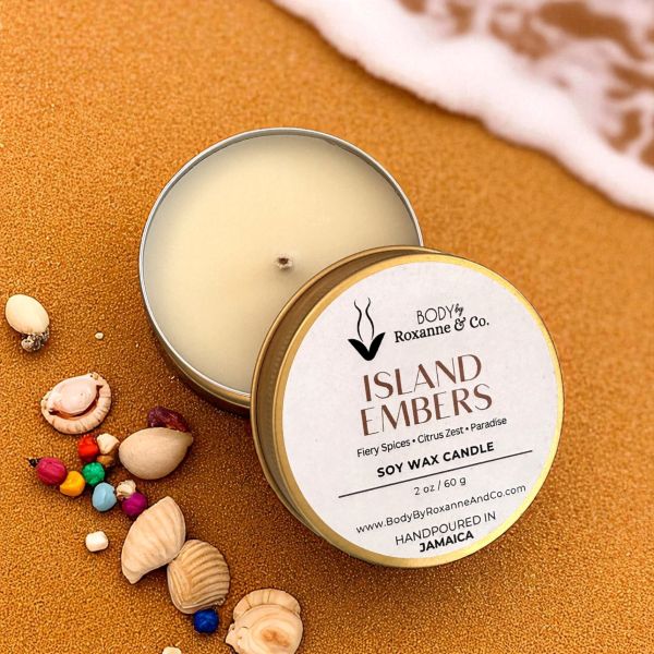Soy wax candle in a tin with 'Body by Roxanne & Co.' branding on a sandy background with shells and beads.